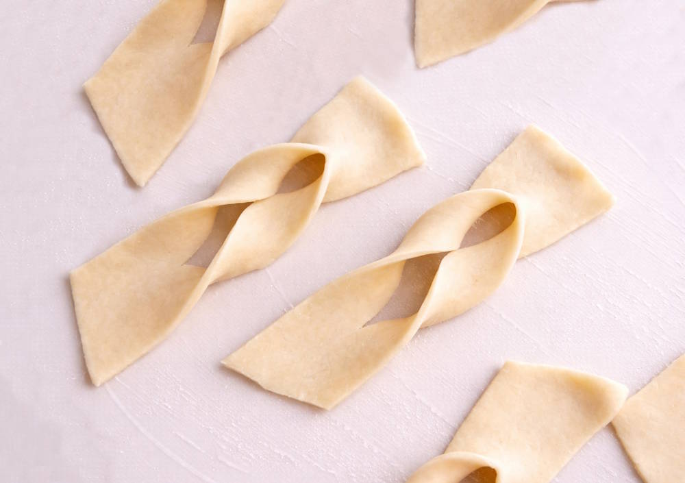 Formowanie faworków – charakterystyczny skręcony kształt Formowanie faworków przez przewlekanie ciasta przez nacięcie