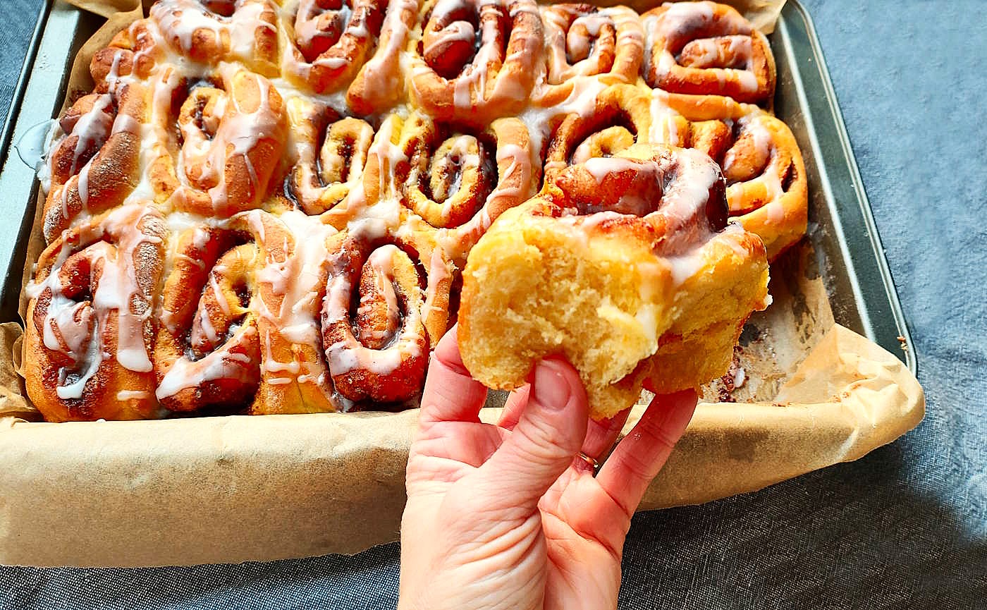 Miękka, świeżo upieczona bułka cynamonowa trzymana w dłoni, widać jej delikatne wnętrze i puszystą strukturę.