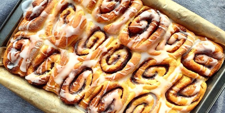 Apetytczne bułki cynamonowe z lukrem przedstawione na blaszce, gotowe do podania – idealne do udostępnienia w social media.