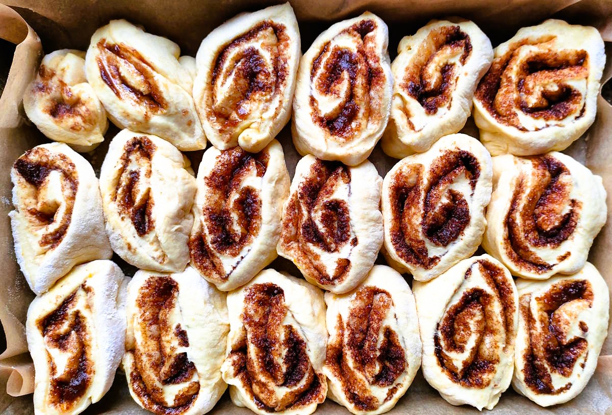 Surowe bułki cynamonowe ułożone obok siebie w blaszce gotowe do wyrastania.