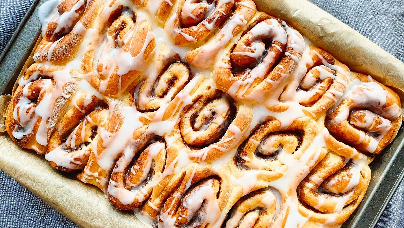 Bułki cynamonowe widziane z góry, świeżo polane lukrem, miękkie i puszyste, ułożone w formie do pieczenia.